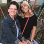 Zwei Frauen auf einem Spielplatz, sitzen auf einer Seilwagen, umgeben von bunten Seilen.