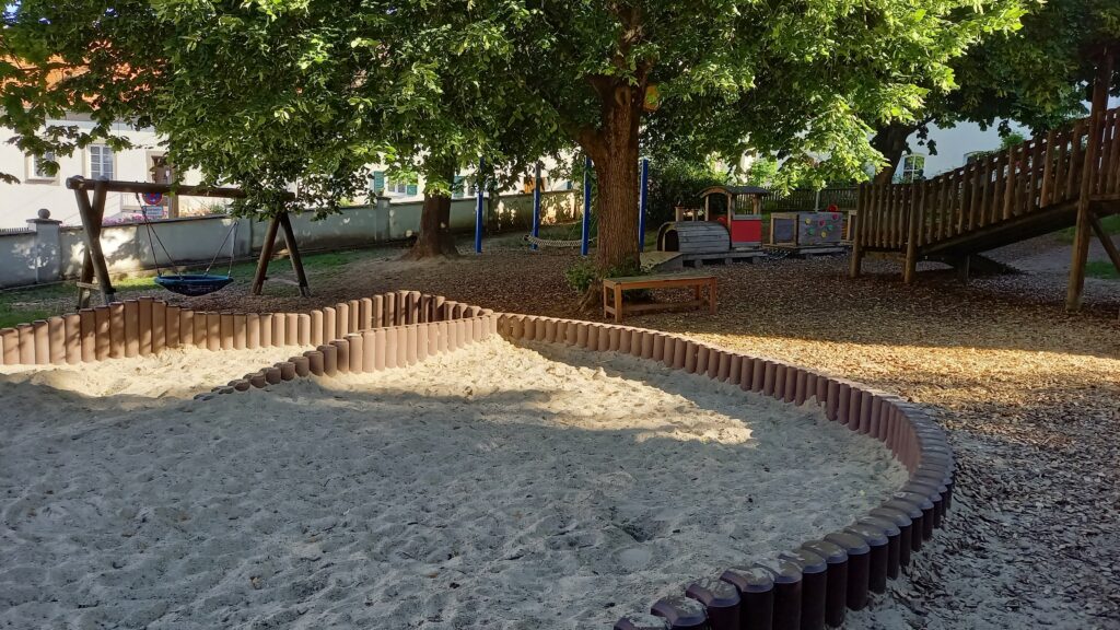 Sandspielplatz mit Kletterwelt und Schaukel im Park.