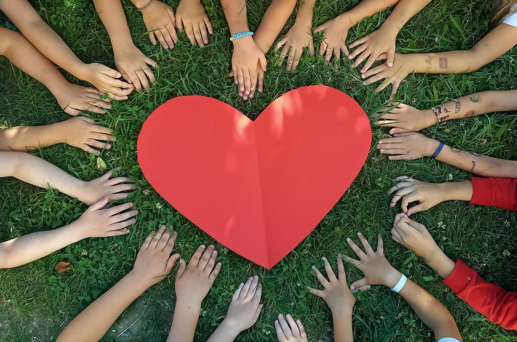 Ein Herz aus Papier mit verschränkten Händen auf grünem Rasen.