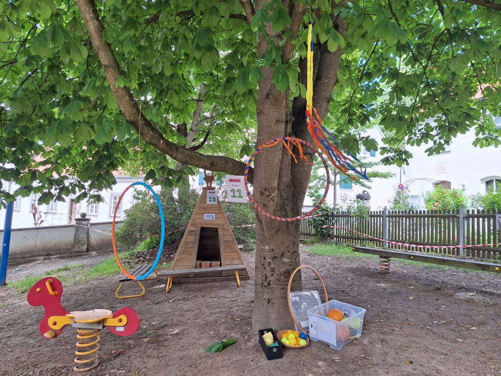 Baum mit Spielplatzgeräten, Hämmer, Kisten und Bändern um einen Baumstamm.