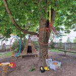 Baum mit Spielplatzgeräten, Hämmer, Kisten und Bändern um einen Baumstamm.