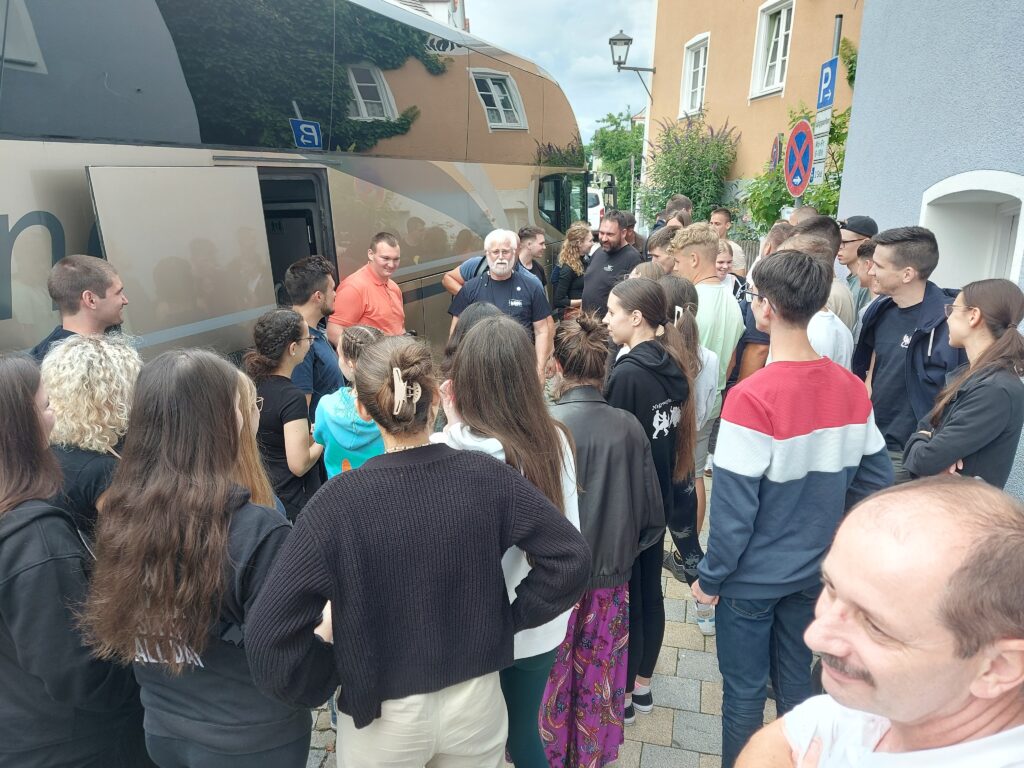 Gruppe Menschen vor Bus auf einem Platz.
