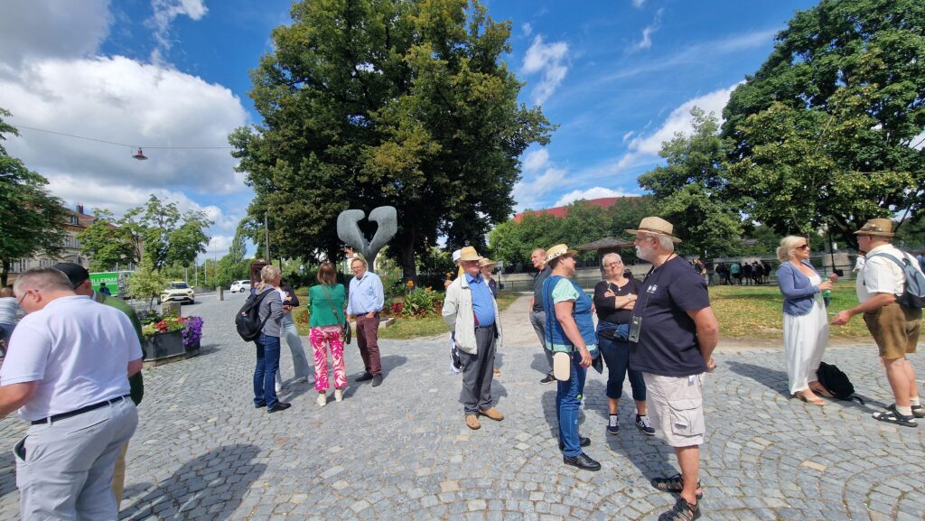 Gruppe von Menschen auf gepflastertem Platz, um einen Skulpturensockel herum.
