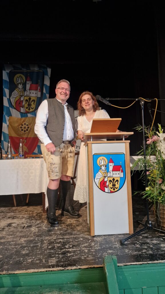 Frau und Mann auf Podium, Marktplatz Altomünster, mit Wappen und traditionellen Kostümen.