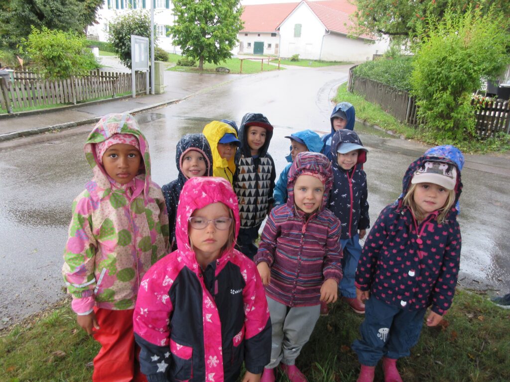 Gruppe von Kindern in Regenbekleidung auf einer nassen Straße.