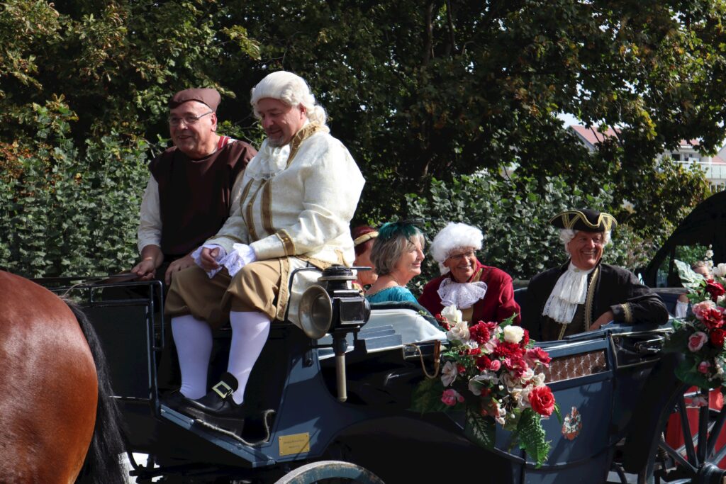 Ein Karren mit Personen in historischen Kostümen, teilweise mit Pferden.