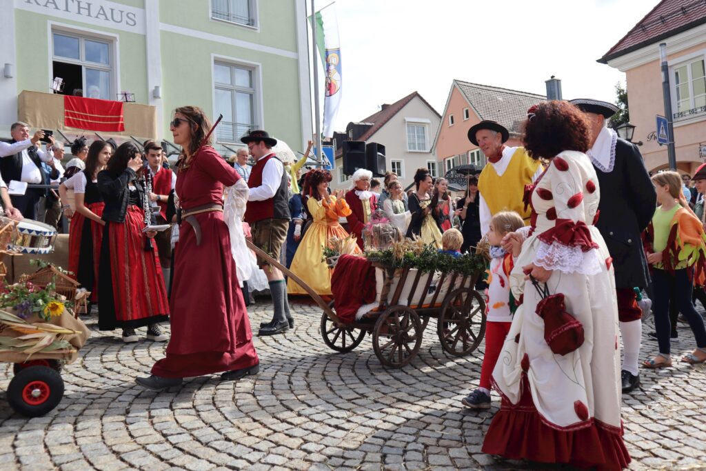 Markt Altomünster: Parade mit traditionellen Kostümen und Karren auf der gepflasterten Straße.