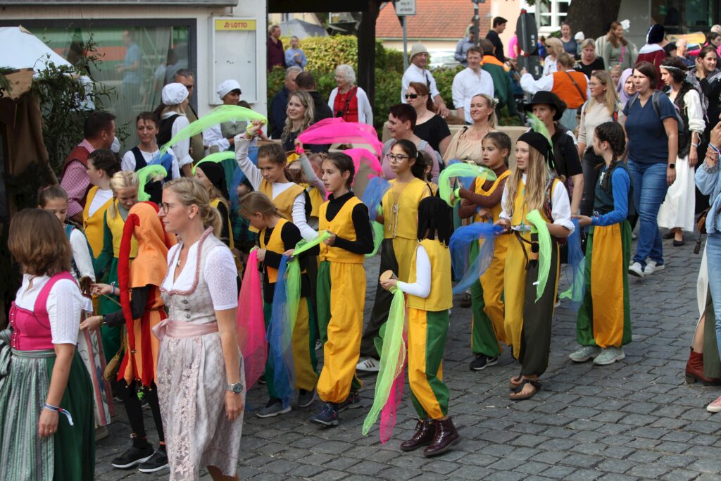 Familien und Jugendliche in farbigen Kostümen auf dem Marktplatz.