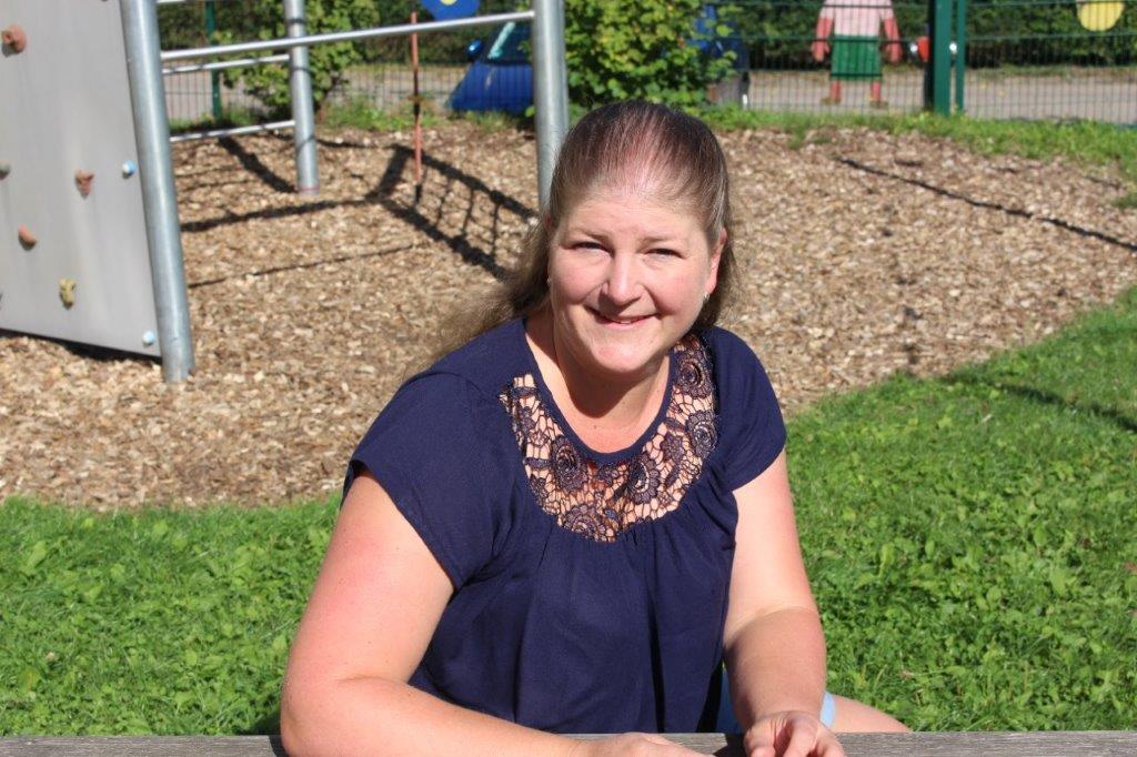 Frau im Freien auf einer Wiese, hinter ihr Spielplatz.