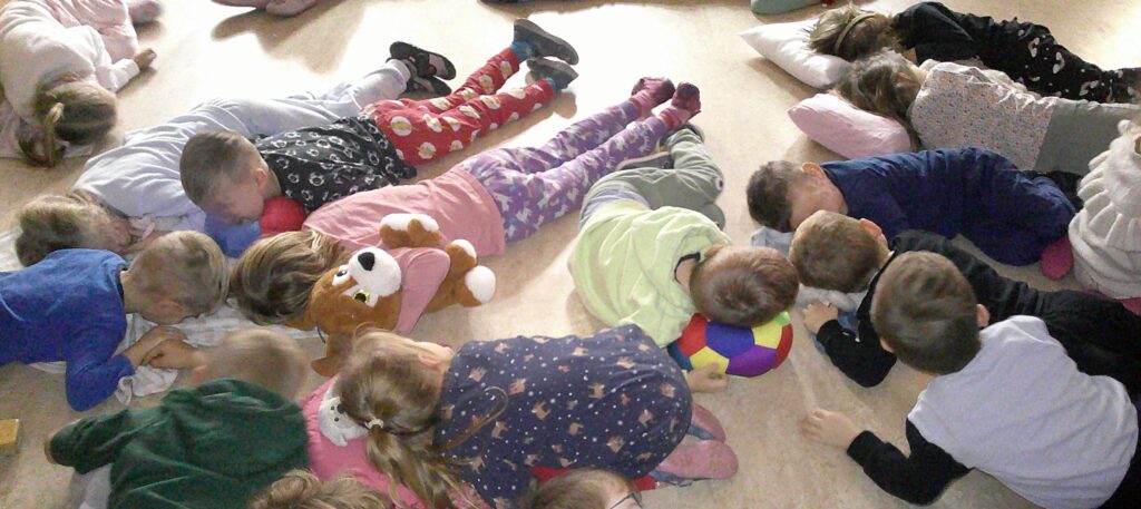 Kinder liegen auf dem Boden, einige mit Plüschtieren und Schutzkissen.