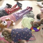 Kinder liegen auf dem Boden, einige mit Plüschtieren und Schutzkissen.