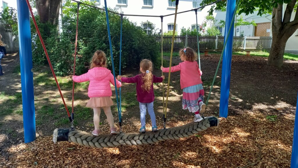 Drei Kinder auf einer Seilrutsche im Spielplatz.