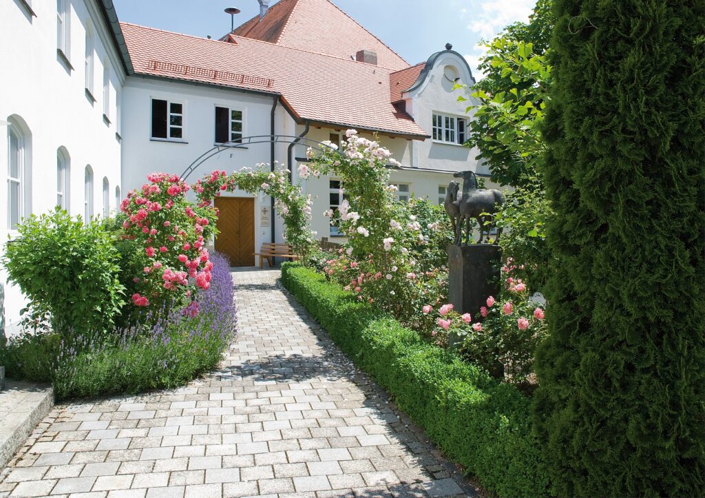 Garten mit Pflanzen und Statue vor weißem Haus.