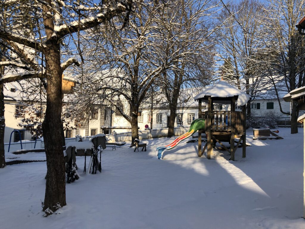 Schneebedeckter Spielplatz mit Winterschein und Bäumen, die sich gegen den klaren Himmel abzeichnen.