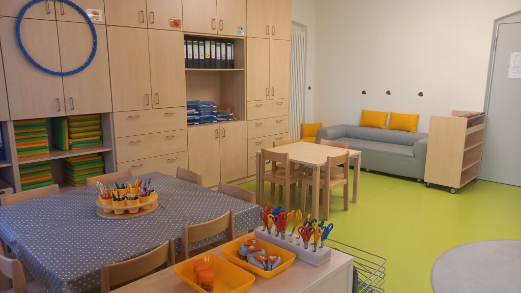 Klassenzimmer mit Tisch, Stühlen, Schneiden, Spielzeuge und Regal.