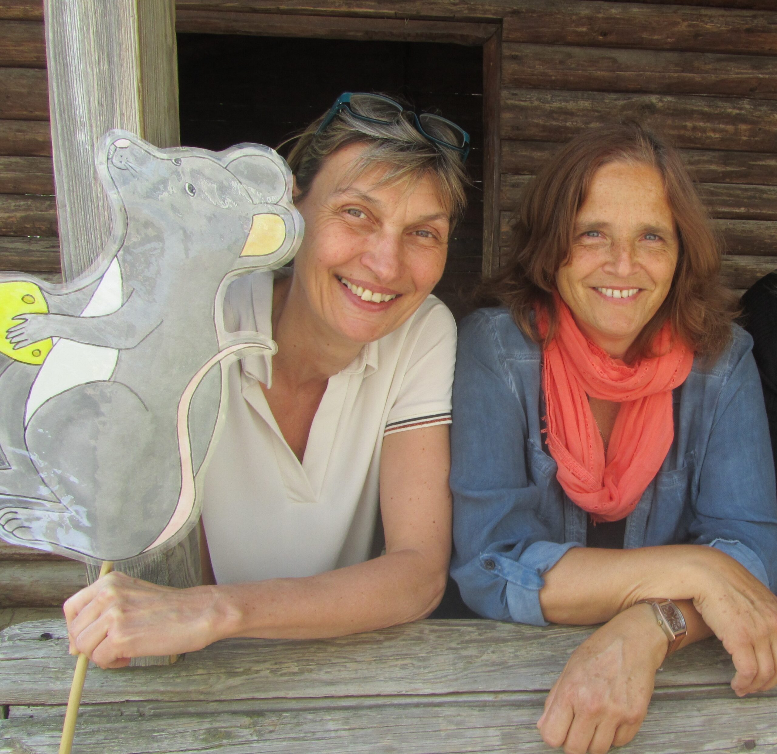 Gruppe Maus Ina und Michaela Zwei Frauen mit einer Mäuse-Plakette vor einer Holzstruktur.