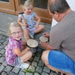 Vater und zwei Mädchen beim Holzwerk auf Pflastersteinen.