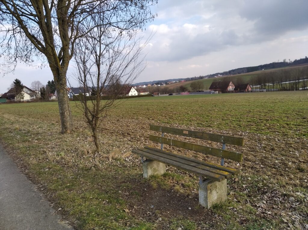 Holzbank in ländlicher Umgebung mit Wegen und Feldern.