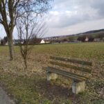 Holzbank in ländlicher Umgebung mit Wegen und Feldern.