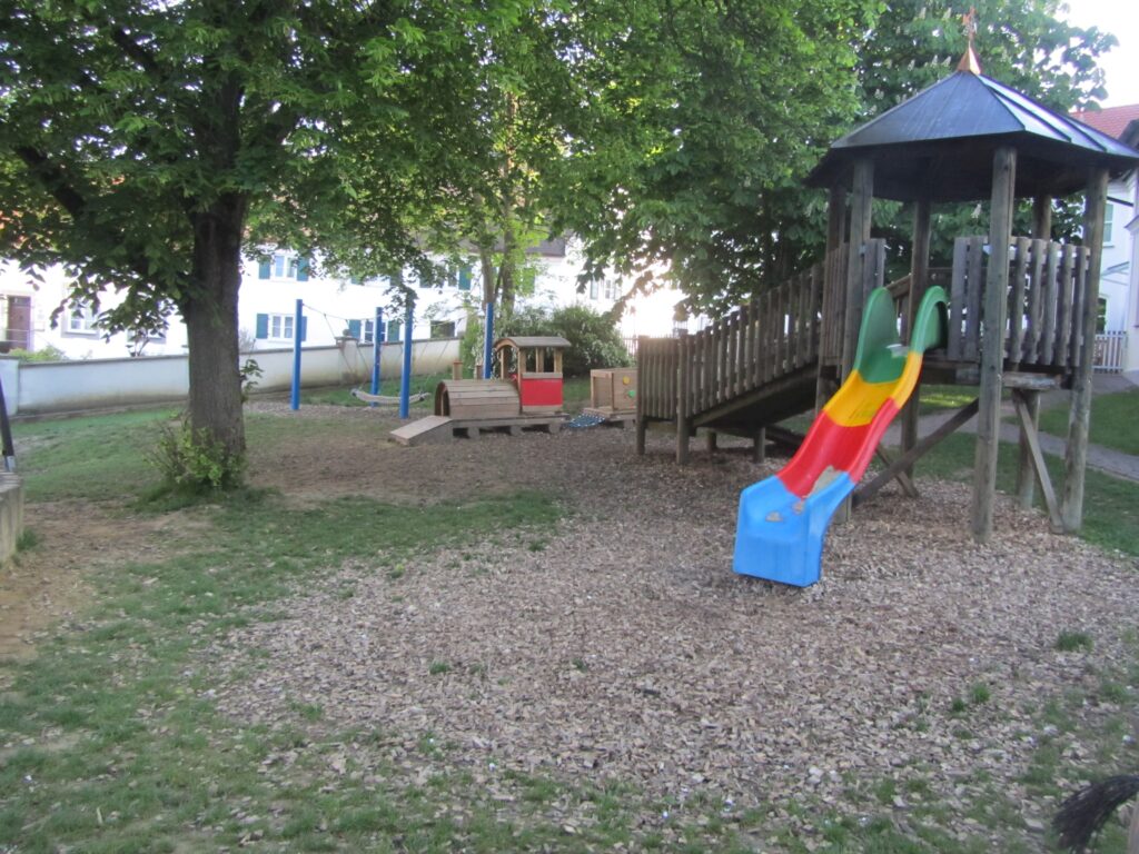 Fußboden mit Holzdecks, Spielplatz mit Wagen, Klettergriffen und Schaukel.