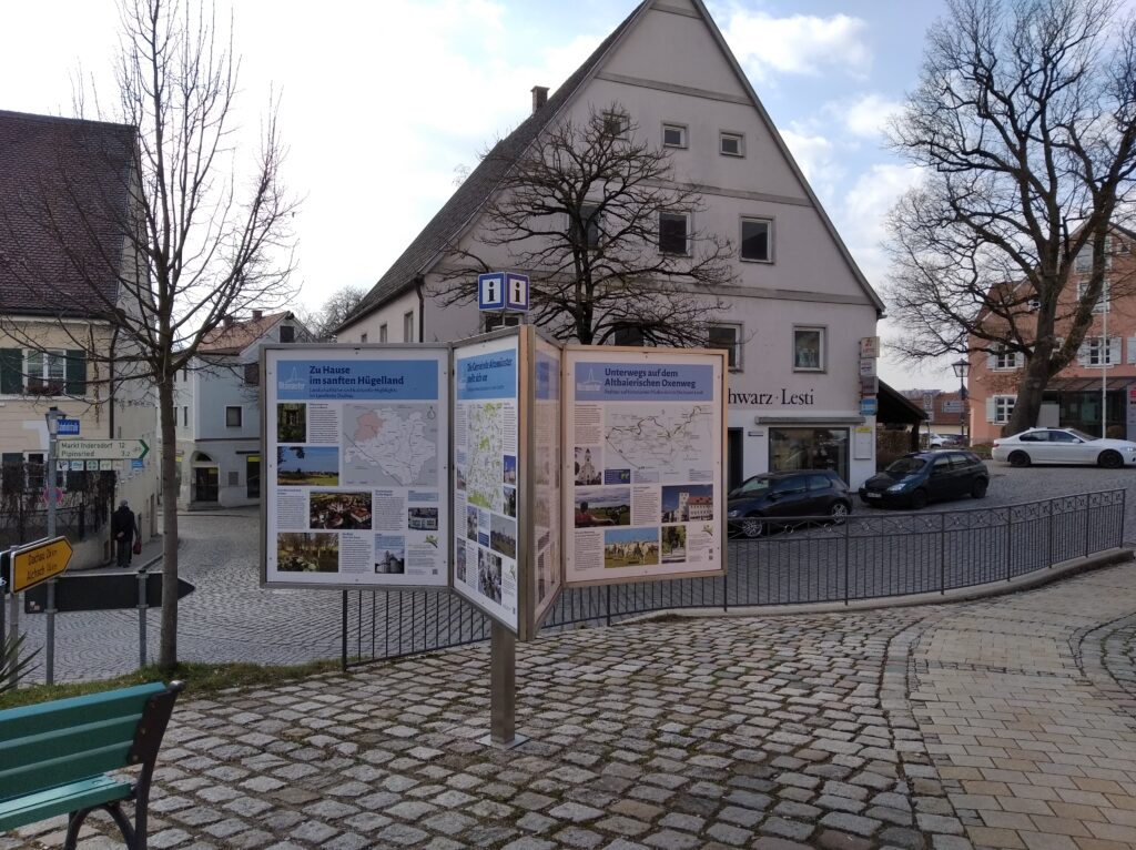 Markt Altomünster, Altstadt mit Gottesdienst, Info-Plakat und gepflasterten Straßen.
