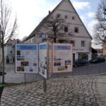 Markt Altomünster, Altstadt mit Gottesdienst, Info-Plakat und gepflasterten Straßen.