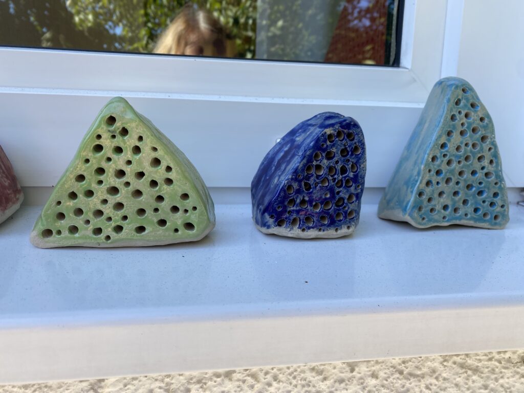 Dreieckige Keramikobjekte mit Löchern auf einem Fensterbrett.