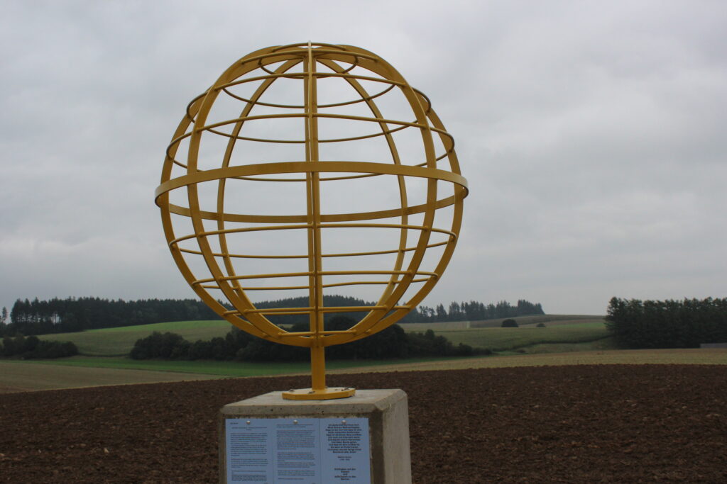 Goldener Globus auf Ackerland, mit Informationspiktogramm.