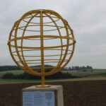 Goldener Globus auf Ackerland, mit Informationspiktogramm.