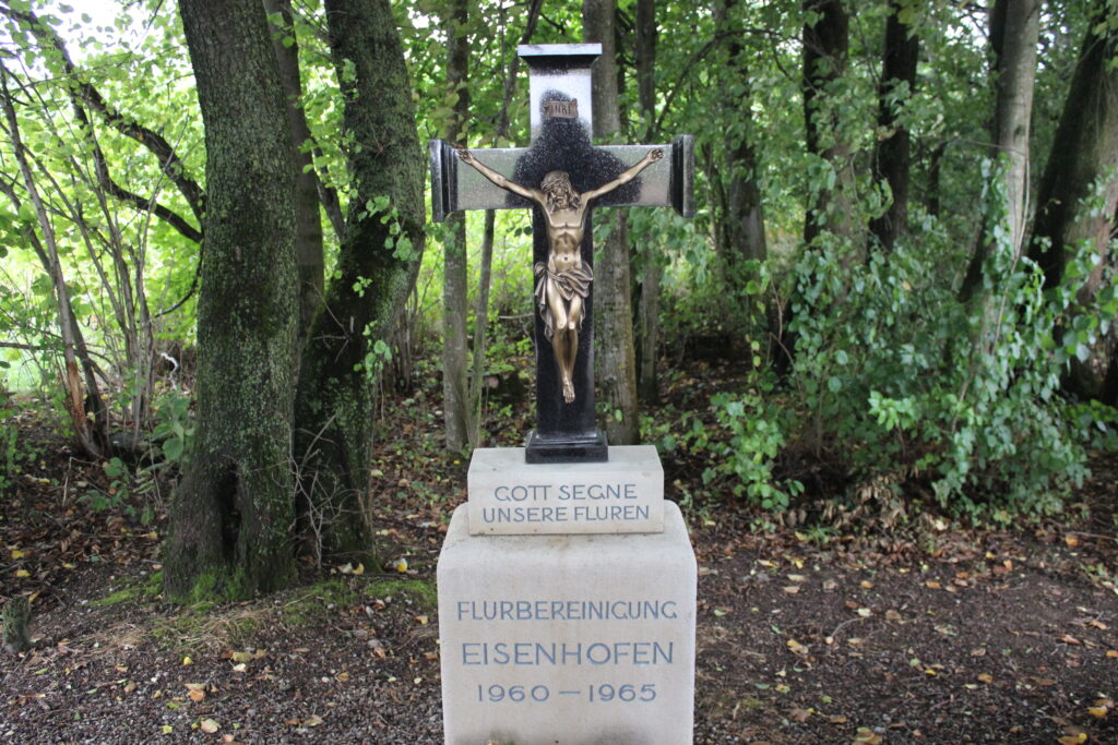 Krug auf Holzstapel, mit Sitz der Flurbereinigung 1960–1965 in Eisenhofen.