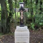 Krug auf Holzstapel, mit Sitz der Flurbereinigung 1960–1965 in Eisenhofen.