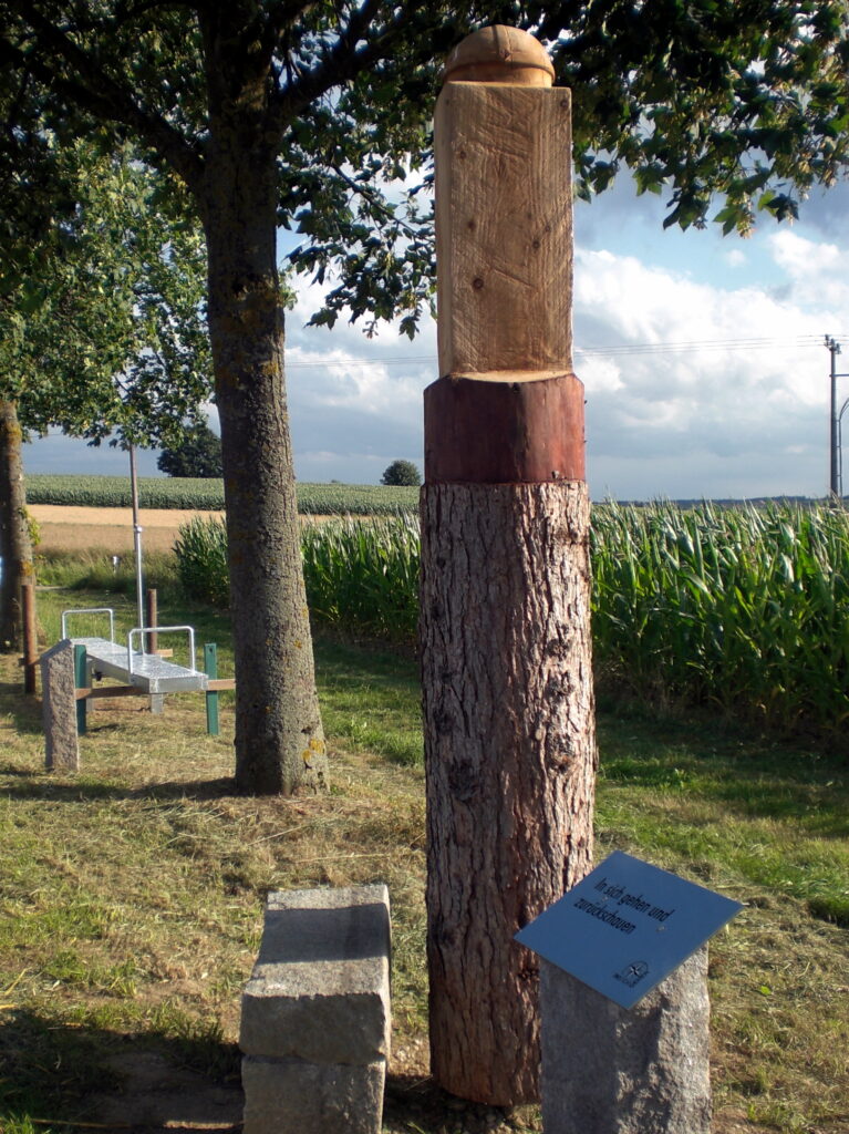 Holzstein mit Sitz und Info-Schild im Gras.