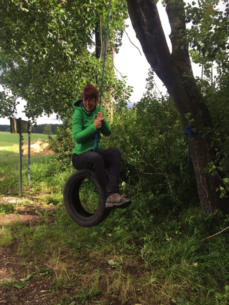 Frau in grüner Jacke auf einem Tire-Swung im Wald.