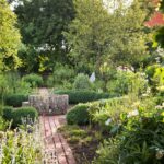 Garten mit Weg, Steinbehälter, Pflanzen und Bäumen.
