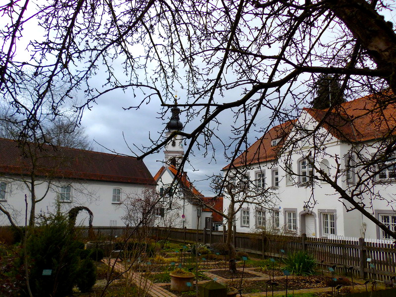 Markt Altomünster mit Kirche und Garten vor bewölktem Himmel.