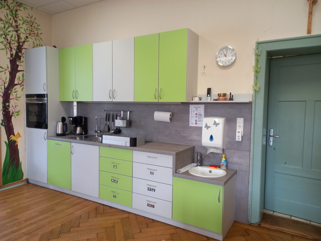 Küchenbereich mit grünen und weißen Schränken, Küchenzeile, Waschbecken und Uhr.