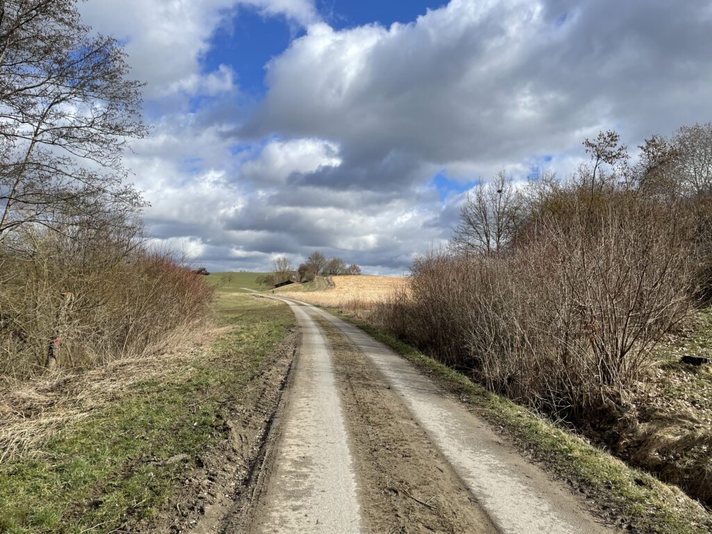 Bergstraße mit unbefestigter Straße und bewölktem Himmel.