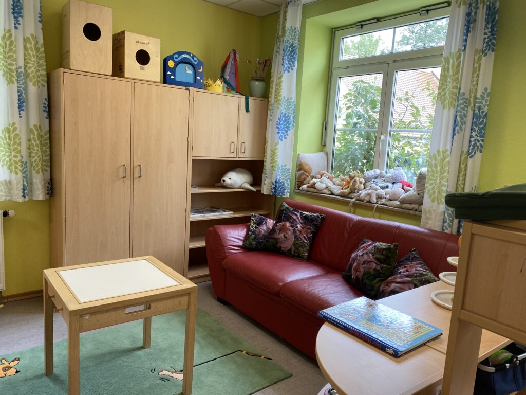 Kindergarten-Raum mit rotem Sofa, Spielzeug und Möbeln.
