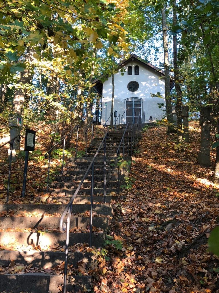 Eine kleine Kirche in der Herde von Altomünster, umgeben von Herbstlaub und Stufen.