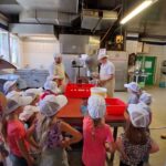 Gruppe von Kindern und Erwachsenen in einer Küchenzeile, die mit Schutzkappen und Kochutensilien arbeitet.
