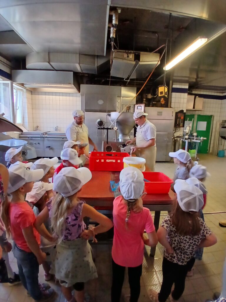 Gruppe von Kindern und Erwachsenen in einer Küchenzeile, die mit Schutzkappen und Kochutensilien arbeitet.