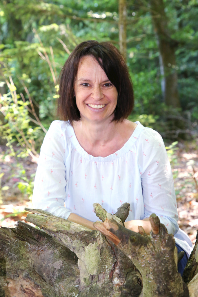 Frau sitzt im Wald mit Baumstamm im Hintergrund.