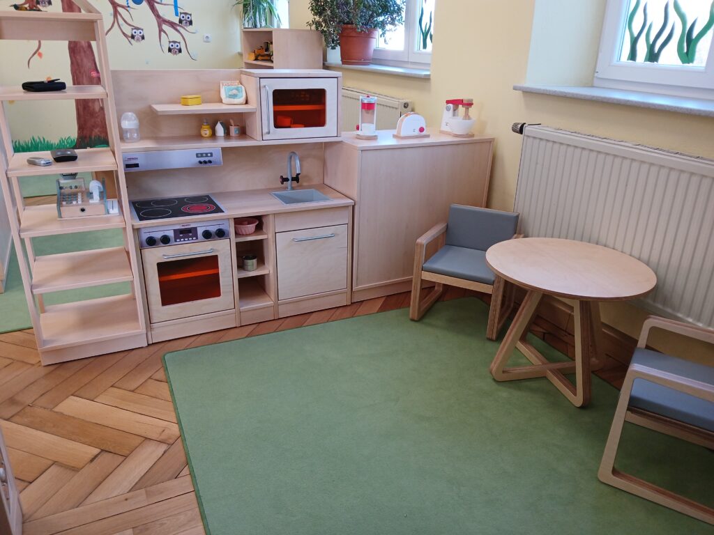 Einfaches Spielzimmer mit Kinderspielküche und Tisch mit Stühlen.
