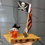 Piratenschiff mit Flagge und Kreatur auf Holzplatte.