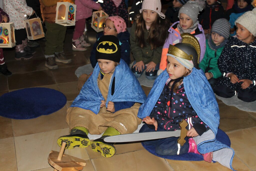 Kinder in Kostümen am Marktplatz, einige mit Lampionen.
