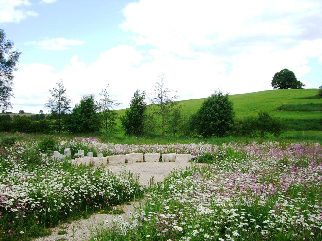 Flussbett mit wilden Blumen und Gras, im Hintergrund Sonnenuhr
