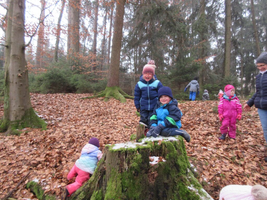 Waldspiele im Herbst, Kinder auf einem Baumstumpf.