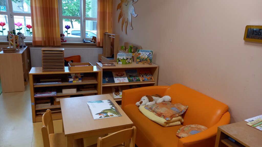 Kindermöbel in einem hellen Raum mit orangefarbenen Akzenten, Stofftiere und Bücher.