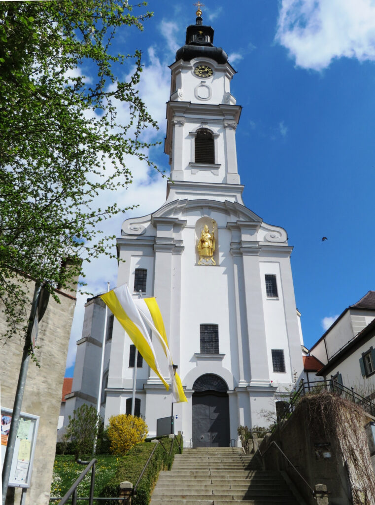 Glockenturm und weißes Kirchengebäude mit gelben Flaggen im Vorgarten.