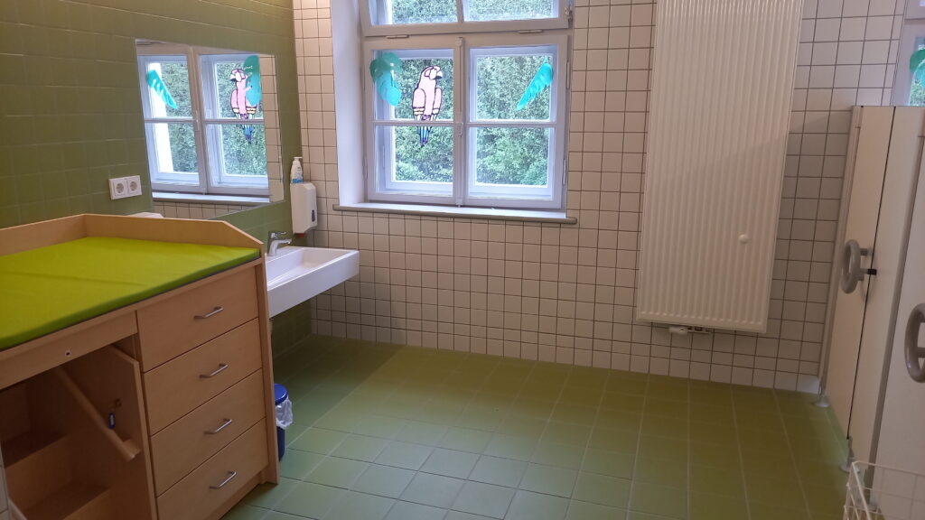 Badezimmer mit Wickelbett, Spüle und Tür.